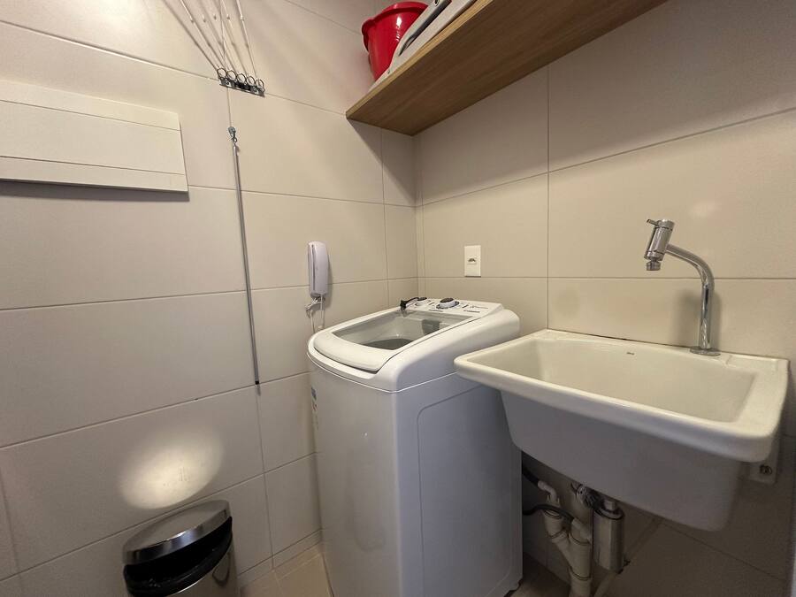 Un baño pequeño con lavadora, lavamanos y un cubo de basura.