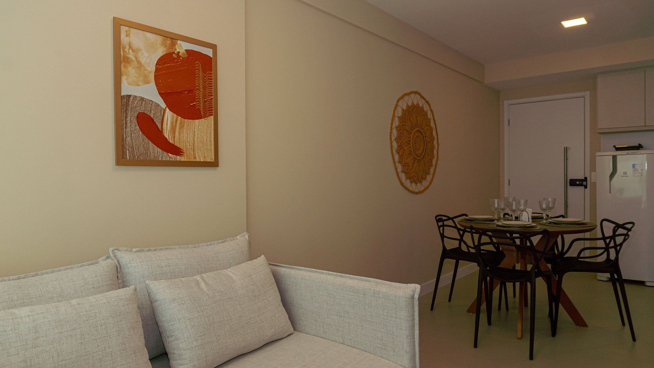 A living room with a sofa, a dining table with chairs, and a kitchen area with a refrigerator.