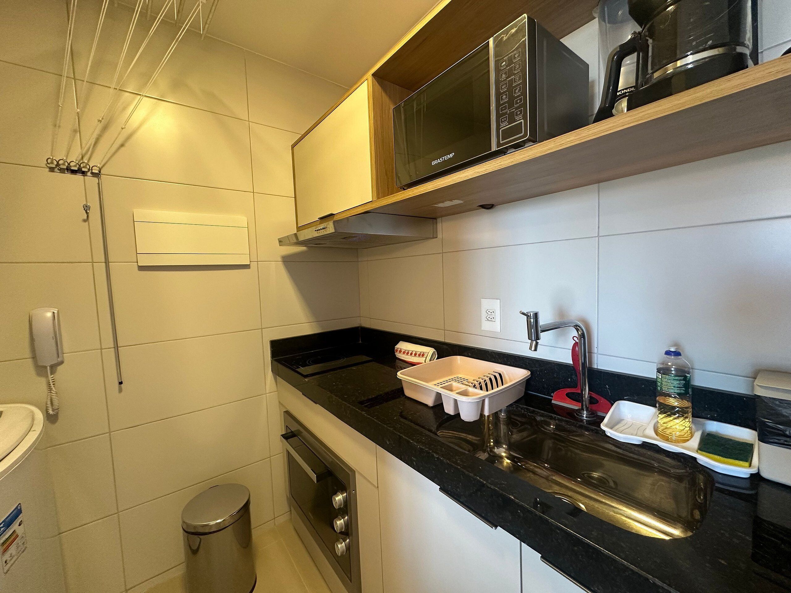 Una cocina compacta con microondas, estufa, fregadero y un pequeño cubo de basura.