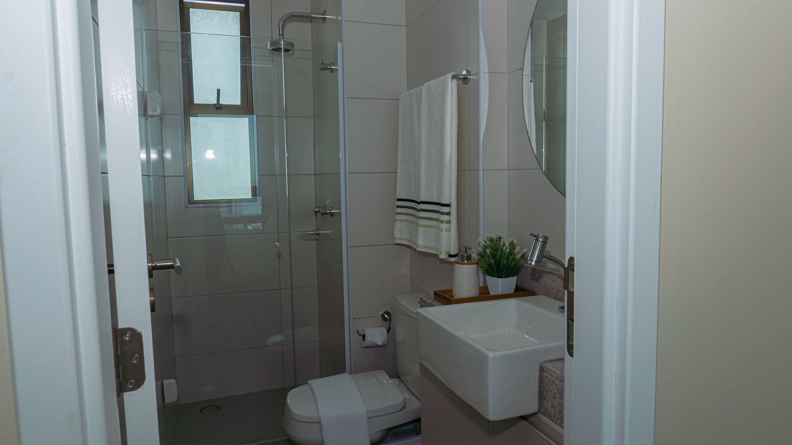 A bathroom with a glass shower enclosure, a toilet, a sink with a mirror above it, and a towel hanging on the wall.