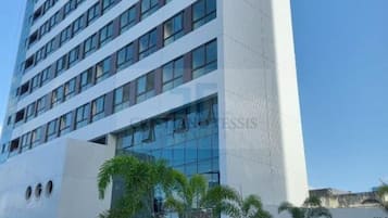 Un hotel moderno de varios pisos con fachada de vidrio, techo plano y entrada ajardinada con palmeras.