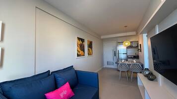 A modern living room with a dark blue sofa, a pink accent pillow, and a dining area with a table and chairs.