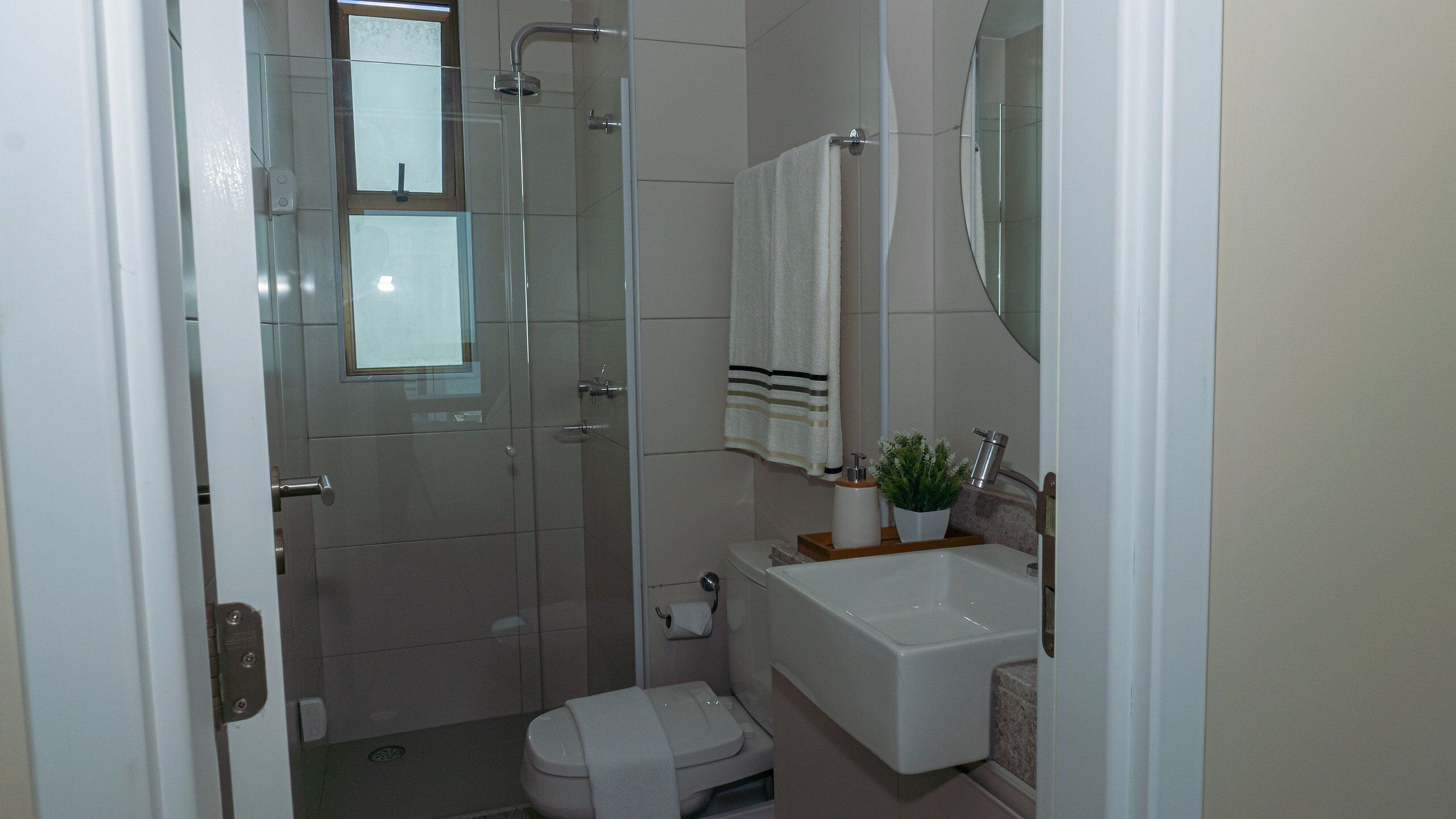 A bathroom with a glass shower enclosure, a toilet, a sink with a mirror above it, and a towel hanging on the wall.