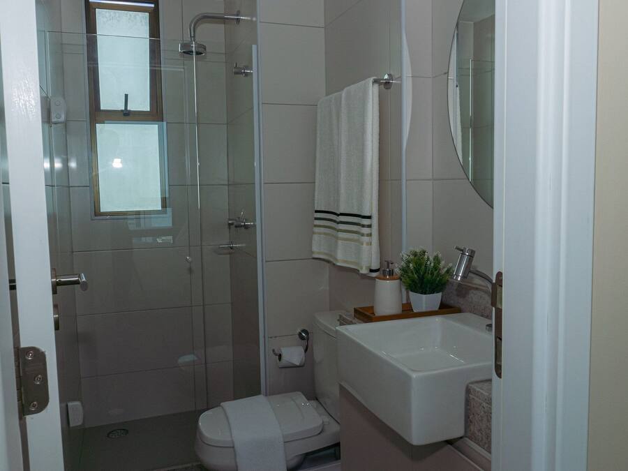 A bathroom with a glass shower enclosure, a toilet, a sink with a mirror above it, and a towel hanging on the wall.