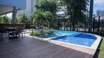 Una piscina con cubierta de madera, barandillas metálicas y mobiliario exterior.