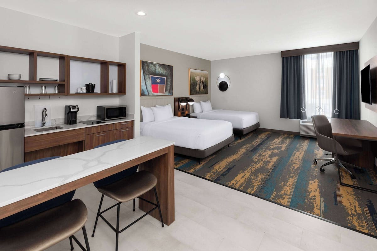 Ein Hotelzimmer mit Küchenzeile, zwei Betten, einem Schreibtisch und einem Fernseher.