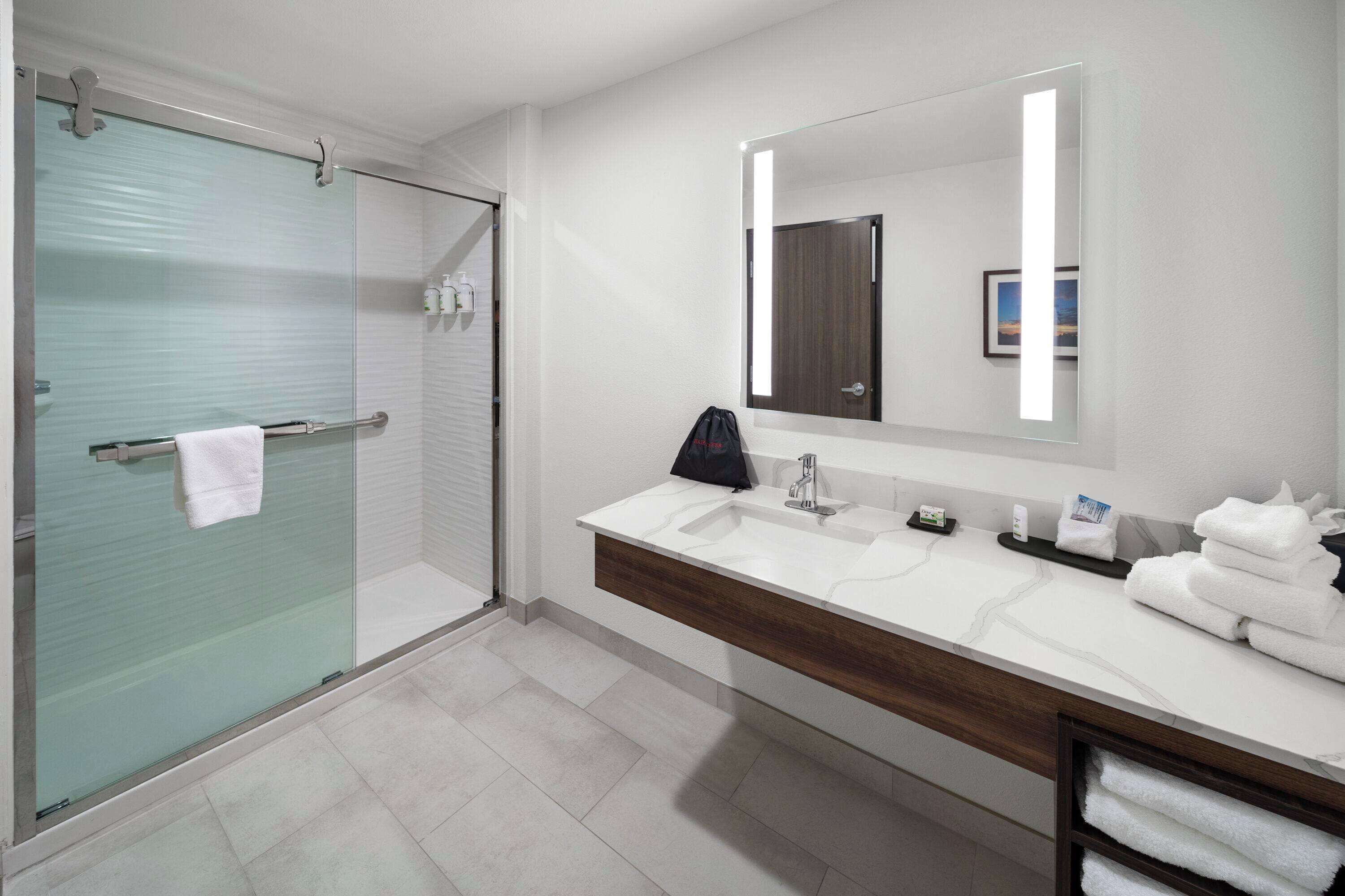 A modern bathroom with a glass shower enclosure, a vanity with a large mirror, and neatly folded towels.