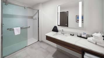 A modern bathroom with a glass shower enclosure, a vanity with a large mirror, and neatly folded towels.