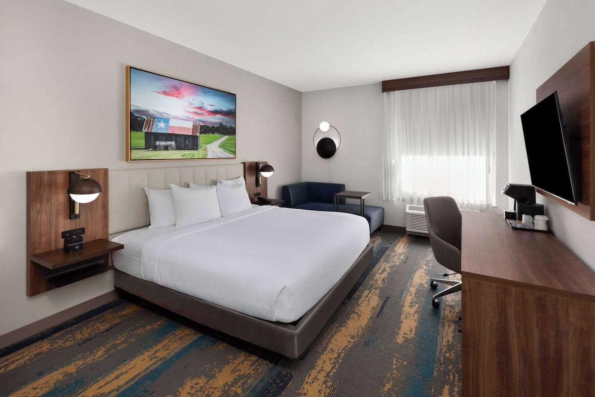 Ein Hotelzimmer mit einem großen Bett, einem Schreibtisch, einem Sessel, einem Fernseher und einem Bild an der Wand.