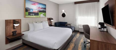 A hotel room with a large bed, a desk, a chair, a TV, and a painting on the wall.