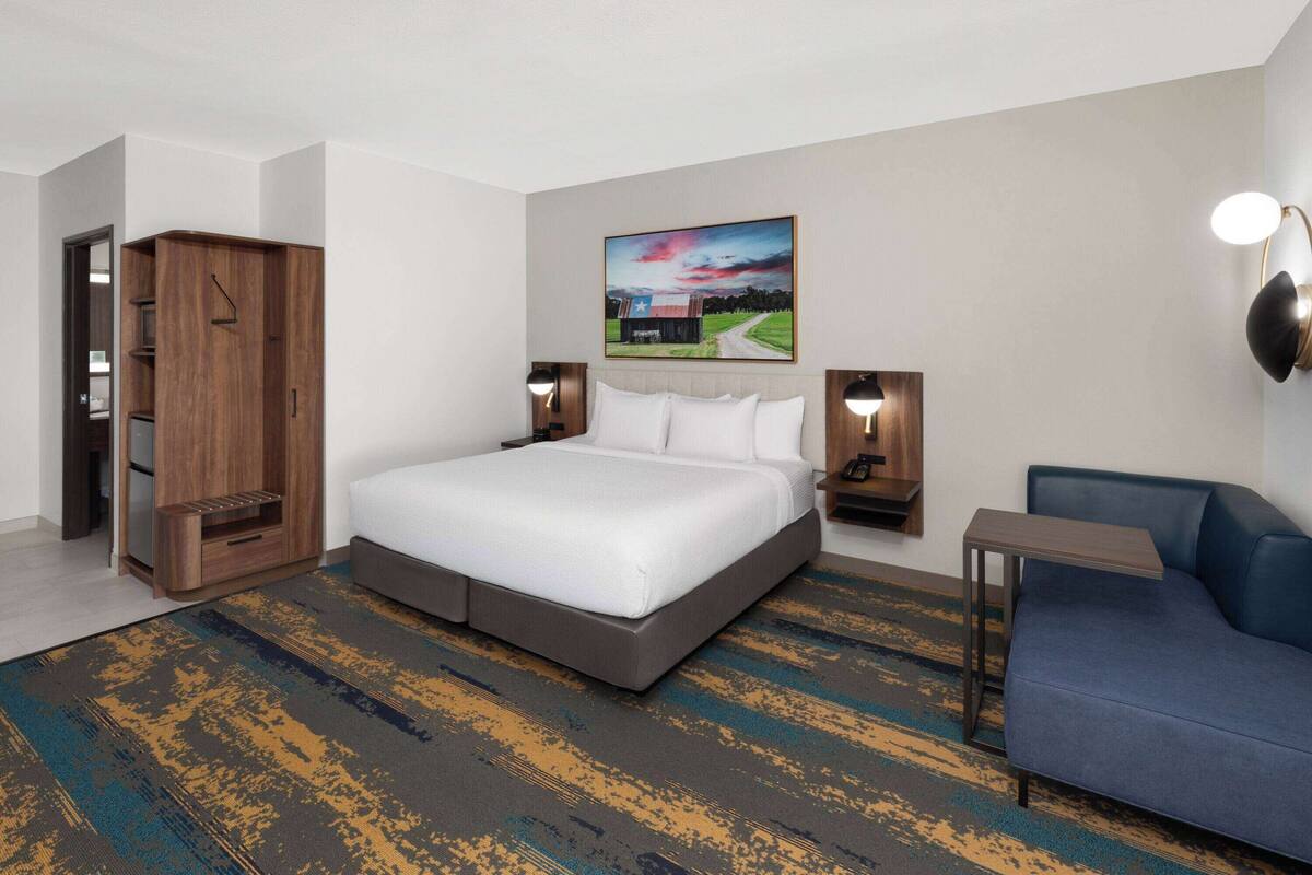 Ein Hotelzimmer mit einem großen Bett, einem blauen Sofa, einem Holzschrank und einem Gemälde an der Wand.