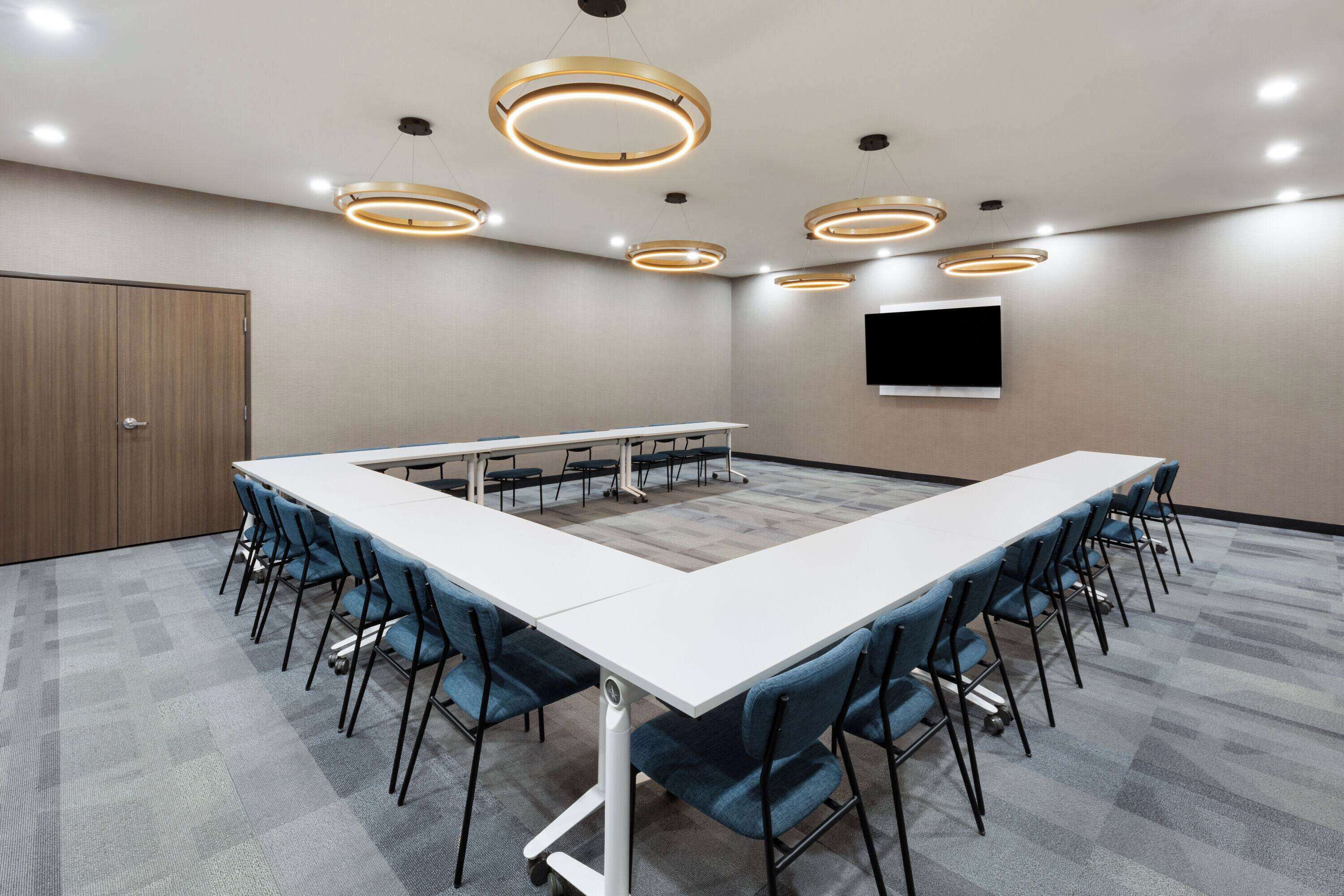 Une salle de conférence avec une longue table, des chaises bleues et des luminaires circulaires au plafond.