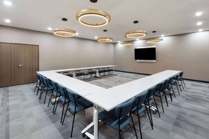 Un salón de conferencias con una larga mesa, sillas azules y luces circulares en el techo.
