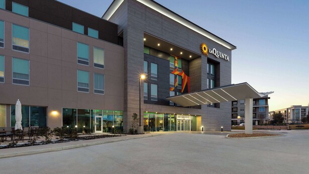 A modern hotel with a prominent sun logo, large windows, and a covered entrance area.