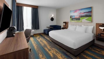 Une chambre d’hôtel avec un grand lit, un bureau, une chaise, une télévision et un tableau au mur.