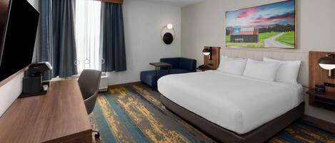 A hotel room with a large bed, a desk, a chair, a TV, and a painting on the wall.