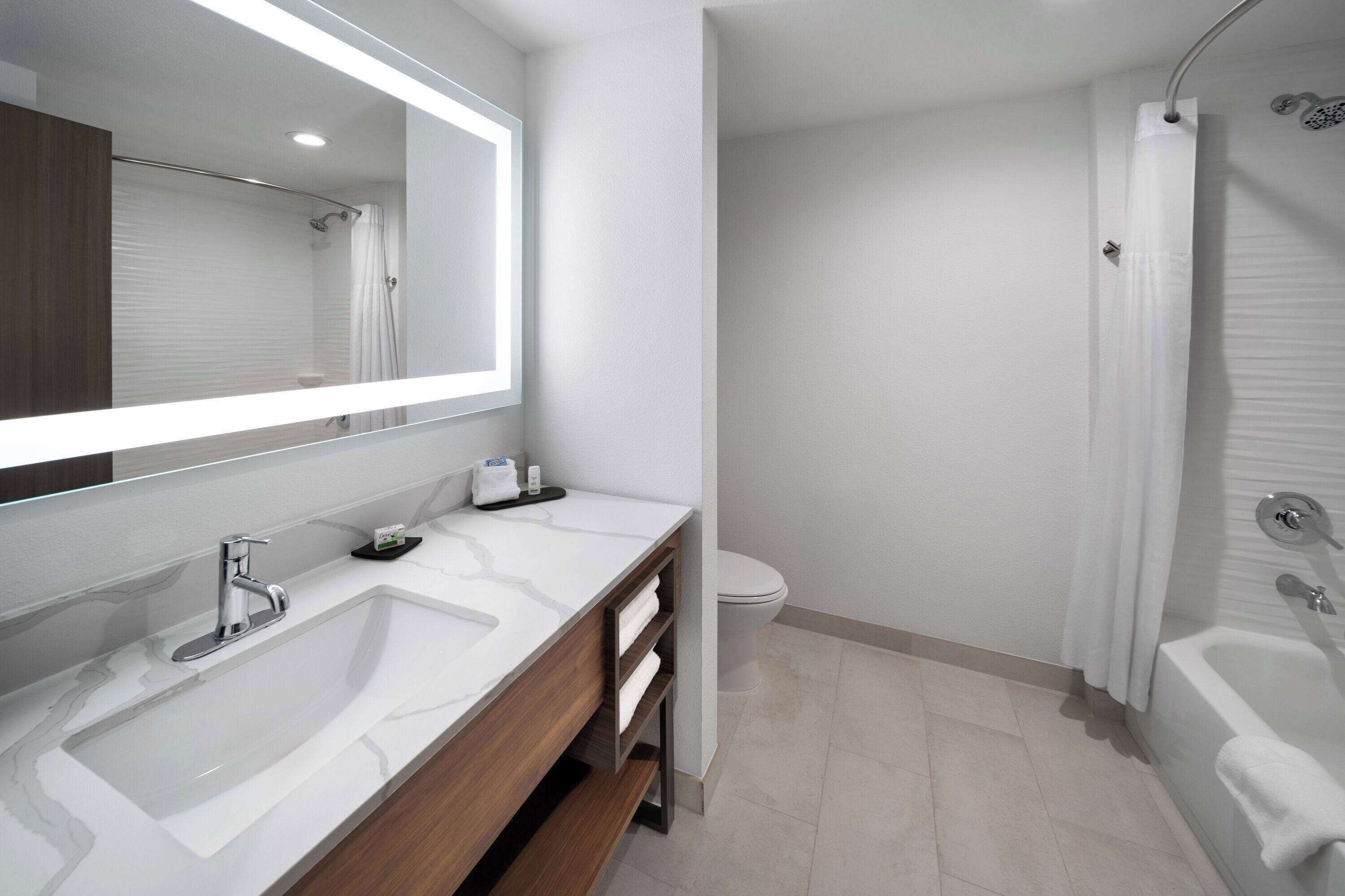 A modern bathroom with a large mirror, two sinks, a shower, and a toilet.