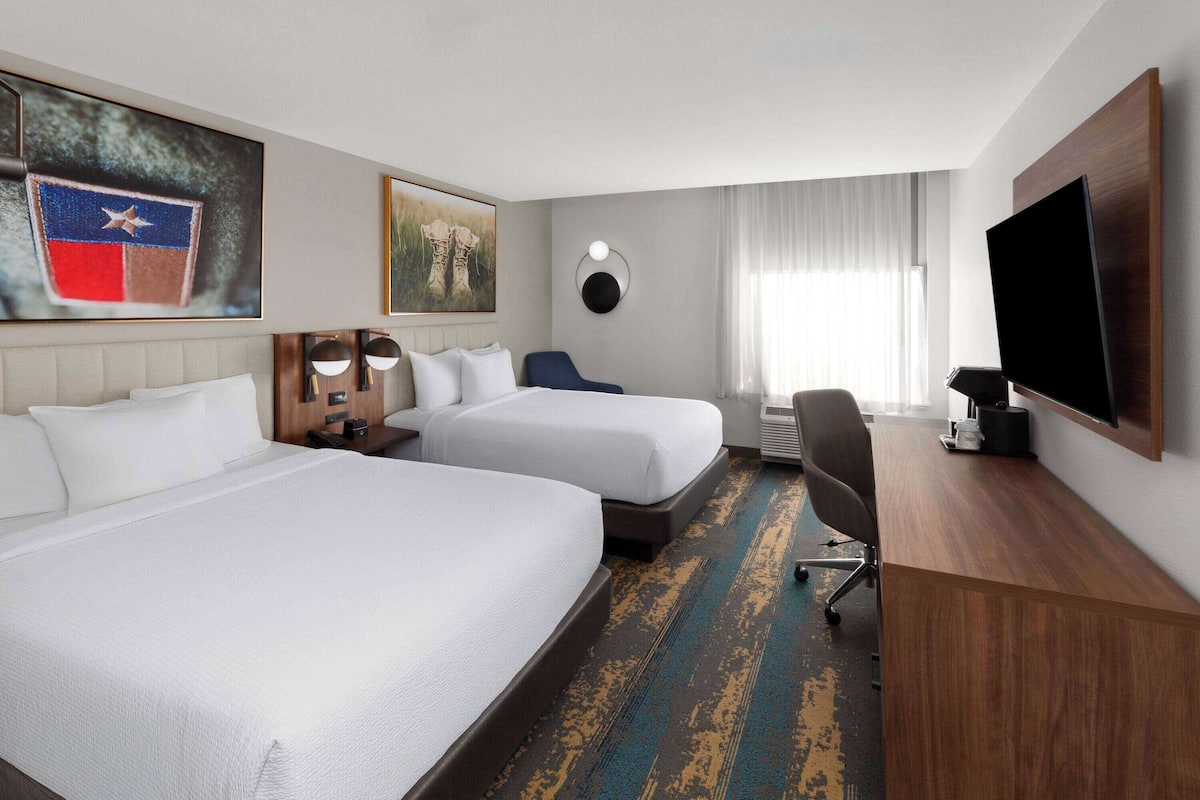 Ein Hotelzimmer mit zwei Betten, einem Schreibtisch, einem Fernseher und Bildern an den Wänden.