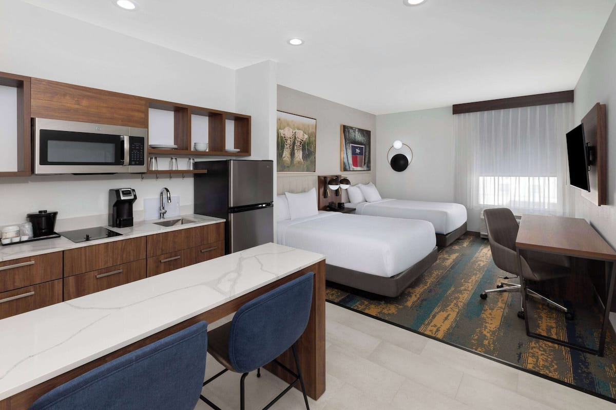 Ein Hotelzimmer mit einer Küchenzeile, einem Bett, einem Schreibtisch und einem Fernseher.