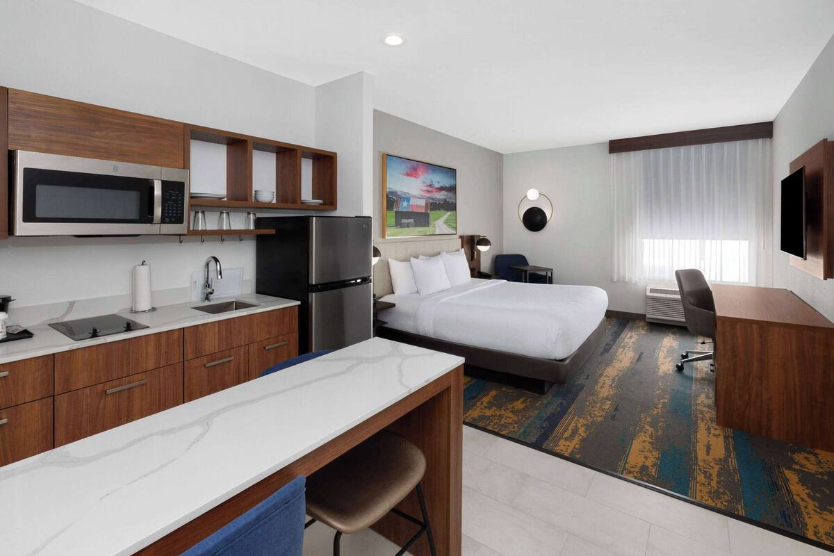 Ein Hotelzimmer mit Bett, Schreibtisch, Küchenzeile und Fernseher.