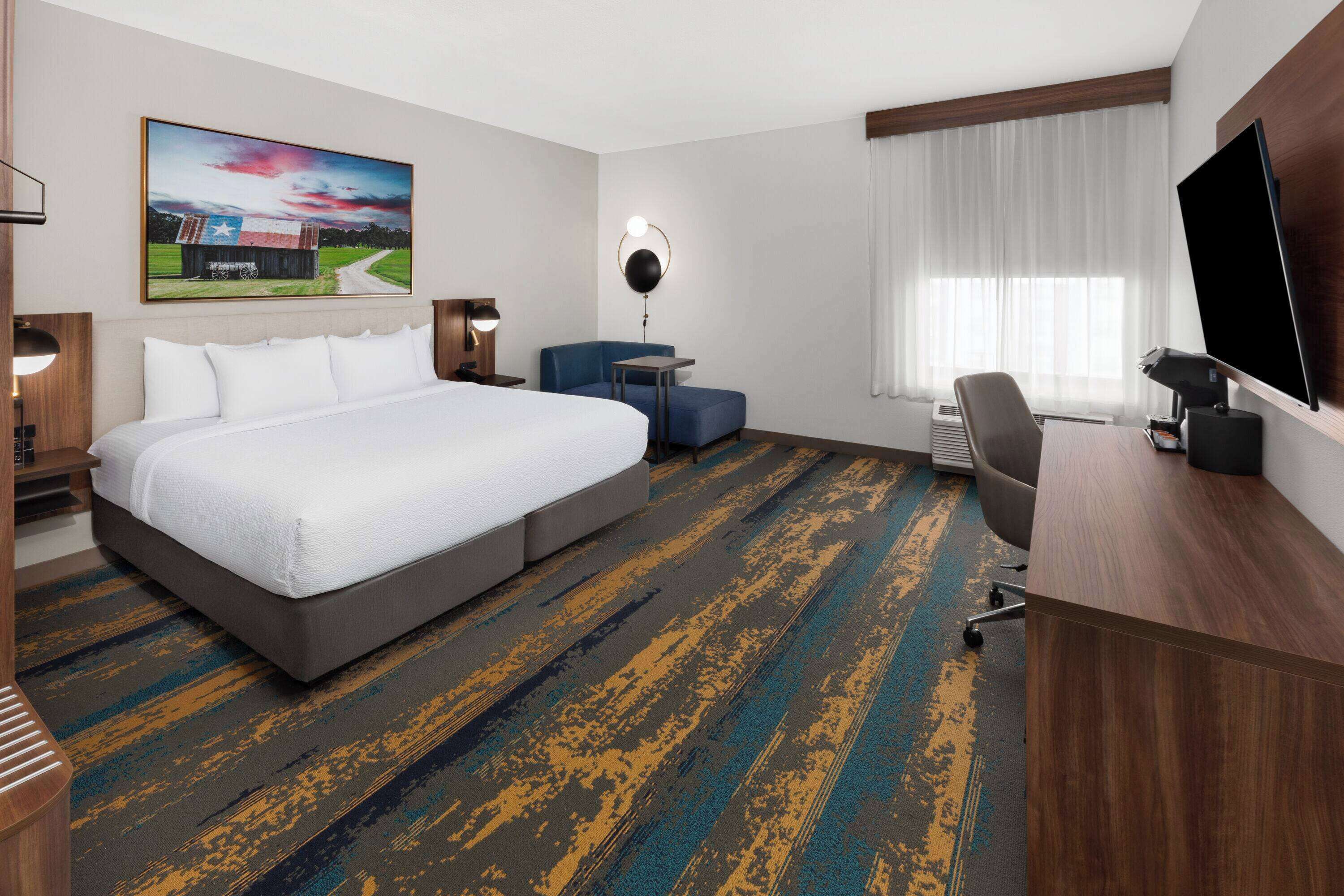Una habitación de hotel con una cama grande, un escritorio, un televisor y un cuadro en la pared.