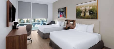 Habitación de hotel con dos camas, un escritorio, una silla, un televisor y ventanas amplias.