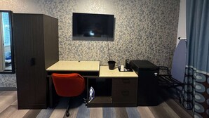 Habitació compacta amb escriptori, cadira, armari i televisió penjada a la paret.