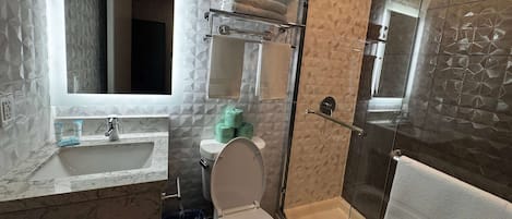 Un baño con lavabo de mármol, inodoro, cabina de ducha con mampara de vidrio y un perchero para toallas.