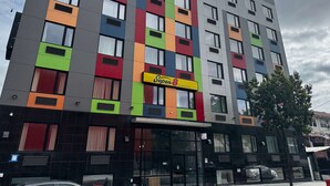 Un edifici de diverses plantes amb façanes de colors, un senyal prominent de 'Super8' i un arbre al davant.