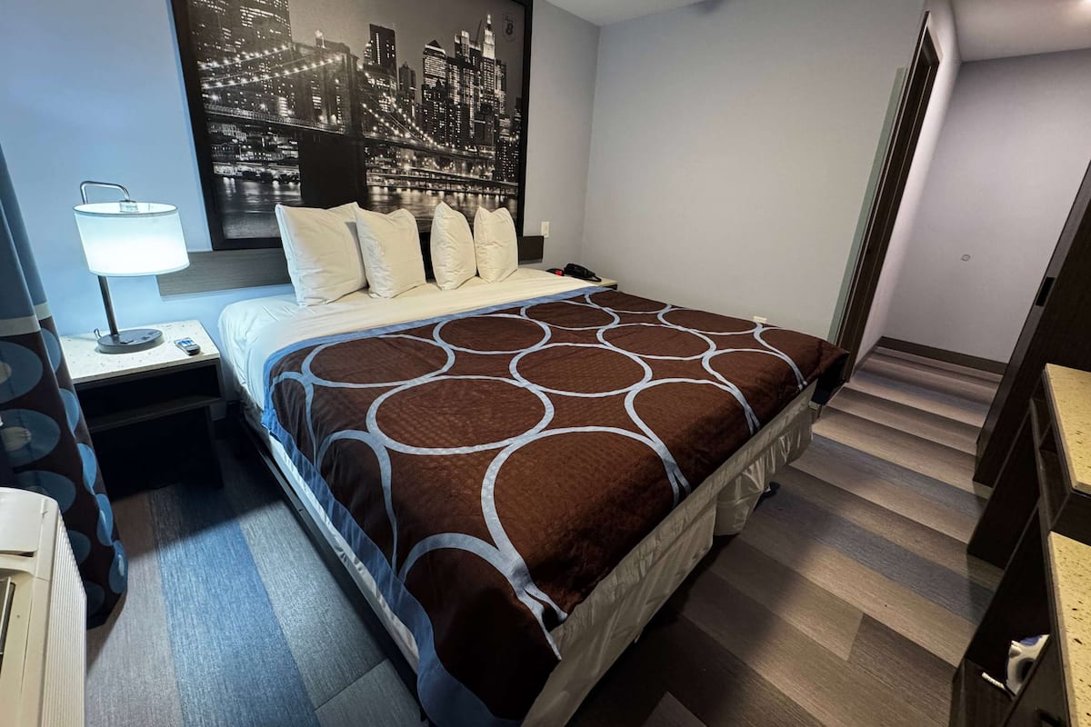 Una habitación de hotel con una cama, una mesita de noche, una lámpara y un cuadro con un paisaje urbano.