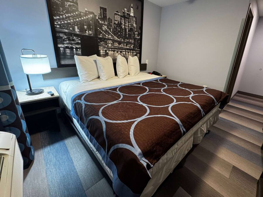 Ein Hotelzimmer mit Bett, Nachttisch, Lampe und Wandbild mit Stadtansicht.