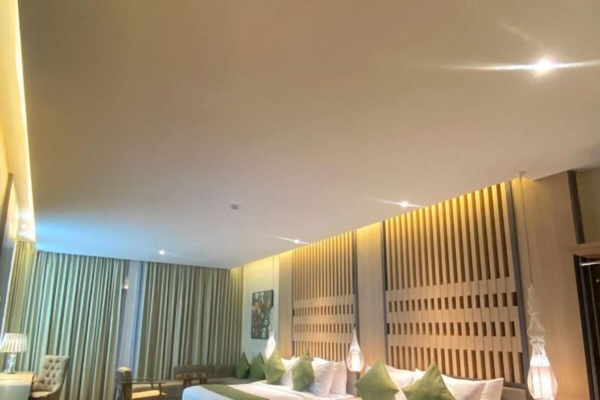 Una habitación de hotel con una cama, una silla, una lámpara y una cortina.