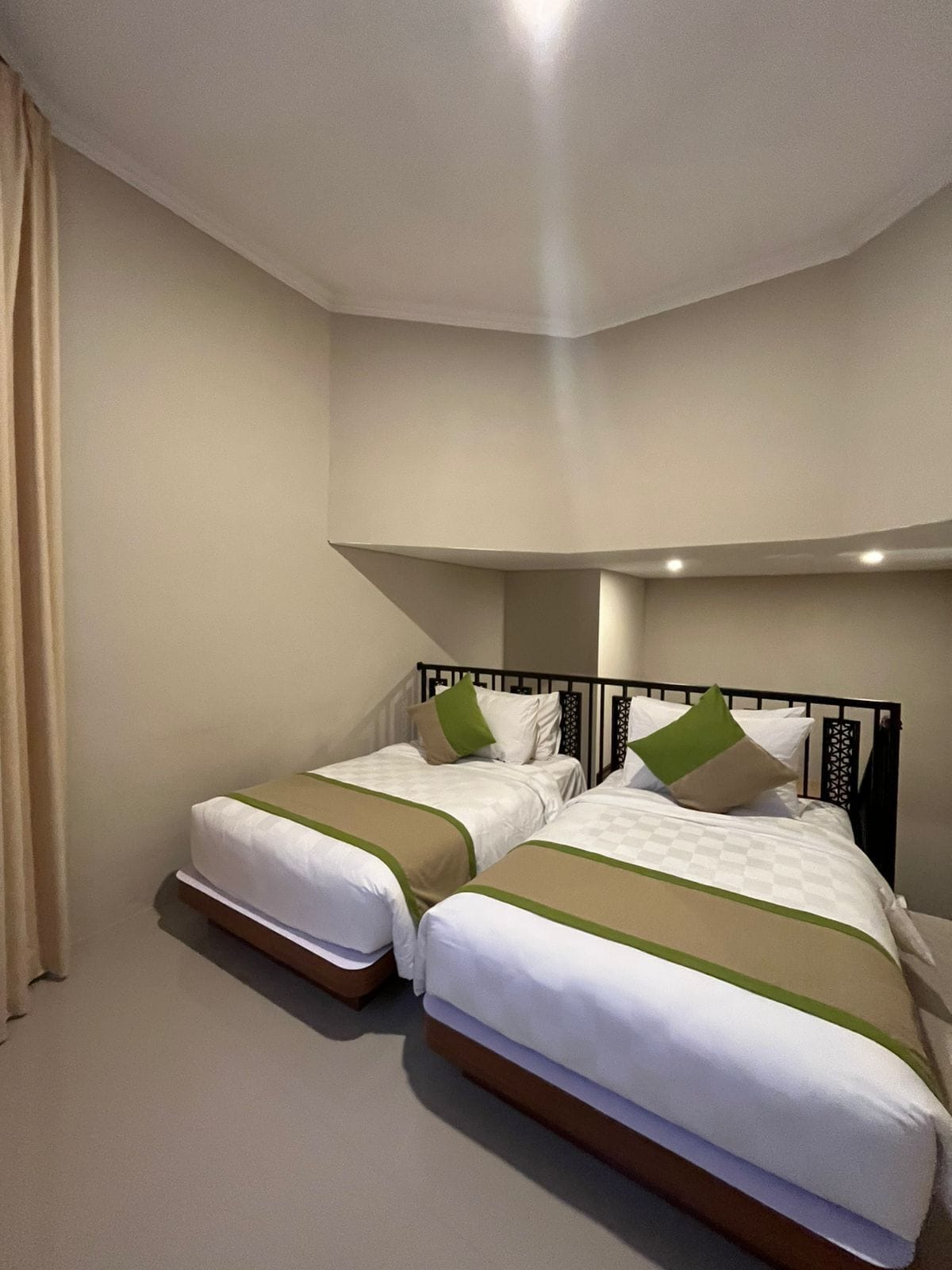 Habitación de hotel con dos camas individuales, paredes color beige y techo curvo.