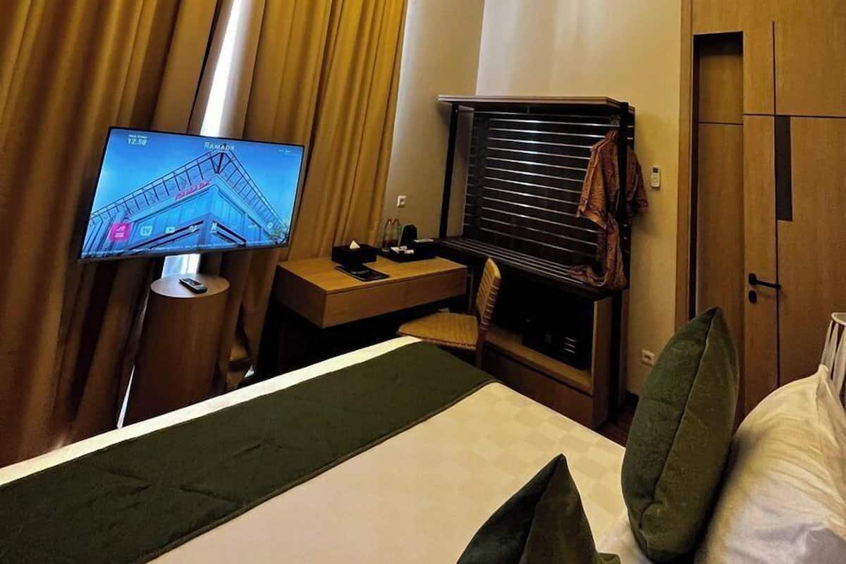 Una habitación de hotel con cama, escritorio, televisión y ventana con cortinas.