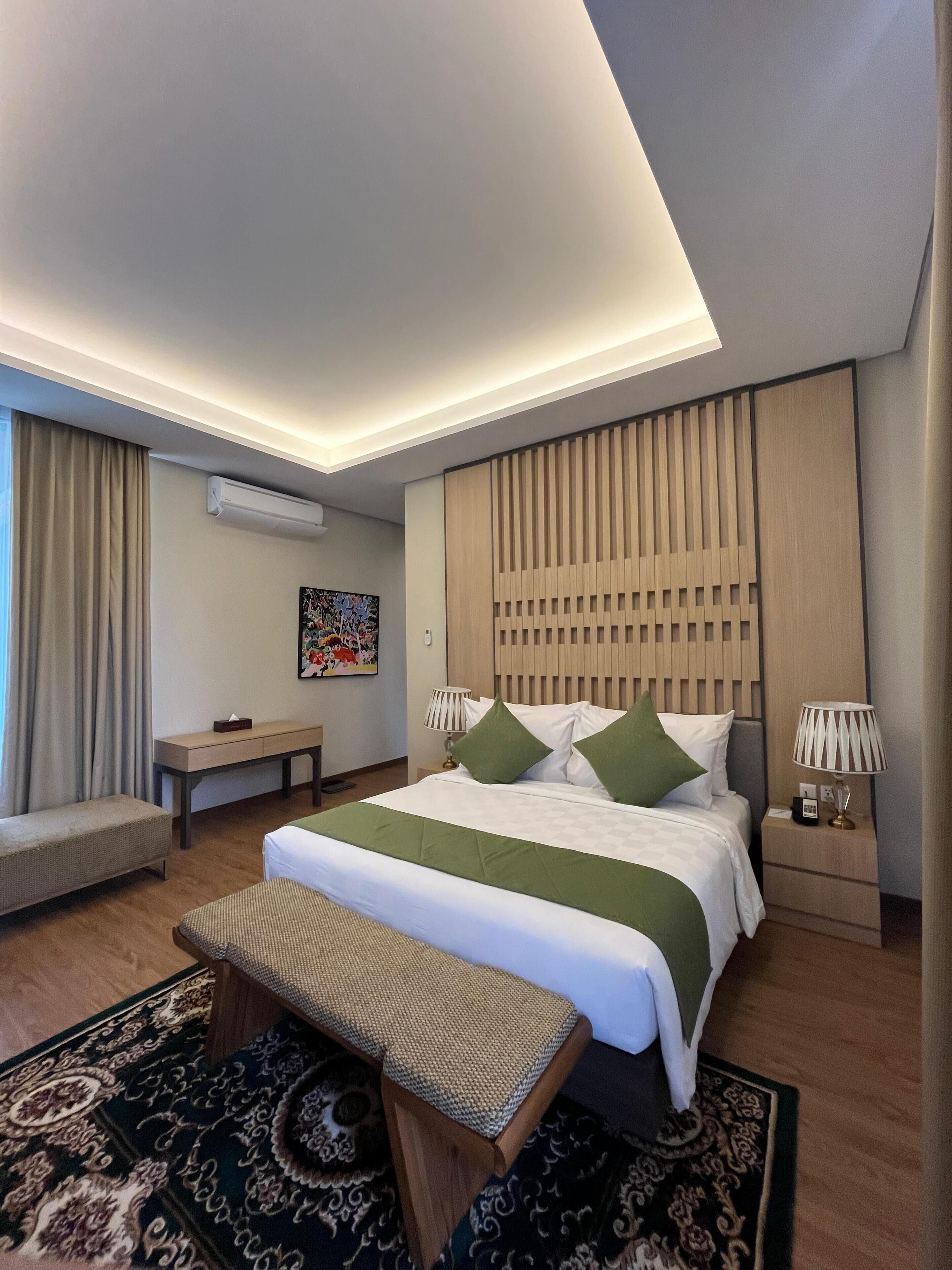 A modern hotel room with a large bed, a bench, a small table, and a patterned rug.