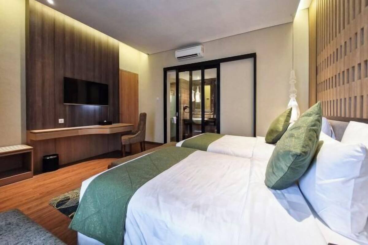 Habitación de hotel con cama, escritorio, televisión y puerta corredera.