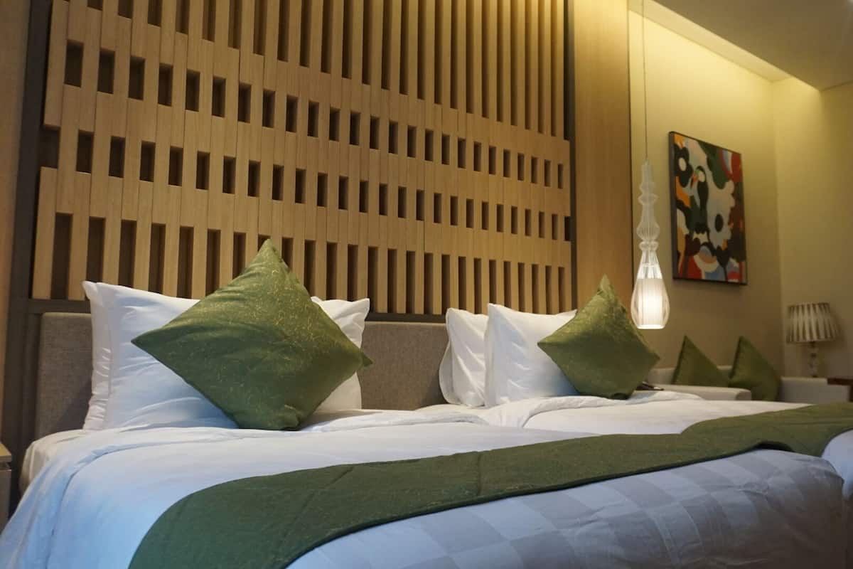 Una habitación de hotel con una cama, almohadas, un panel de pared, un cuadro y una lámpara.