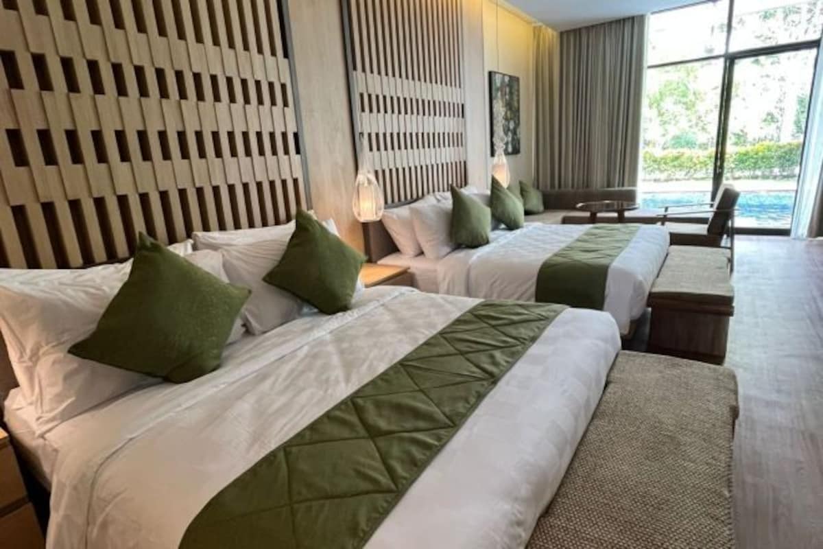 Habitación de hotel con dos camas, cabecera de madera, vistas al exterior y una pequeña mesa.