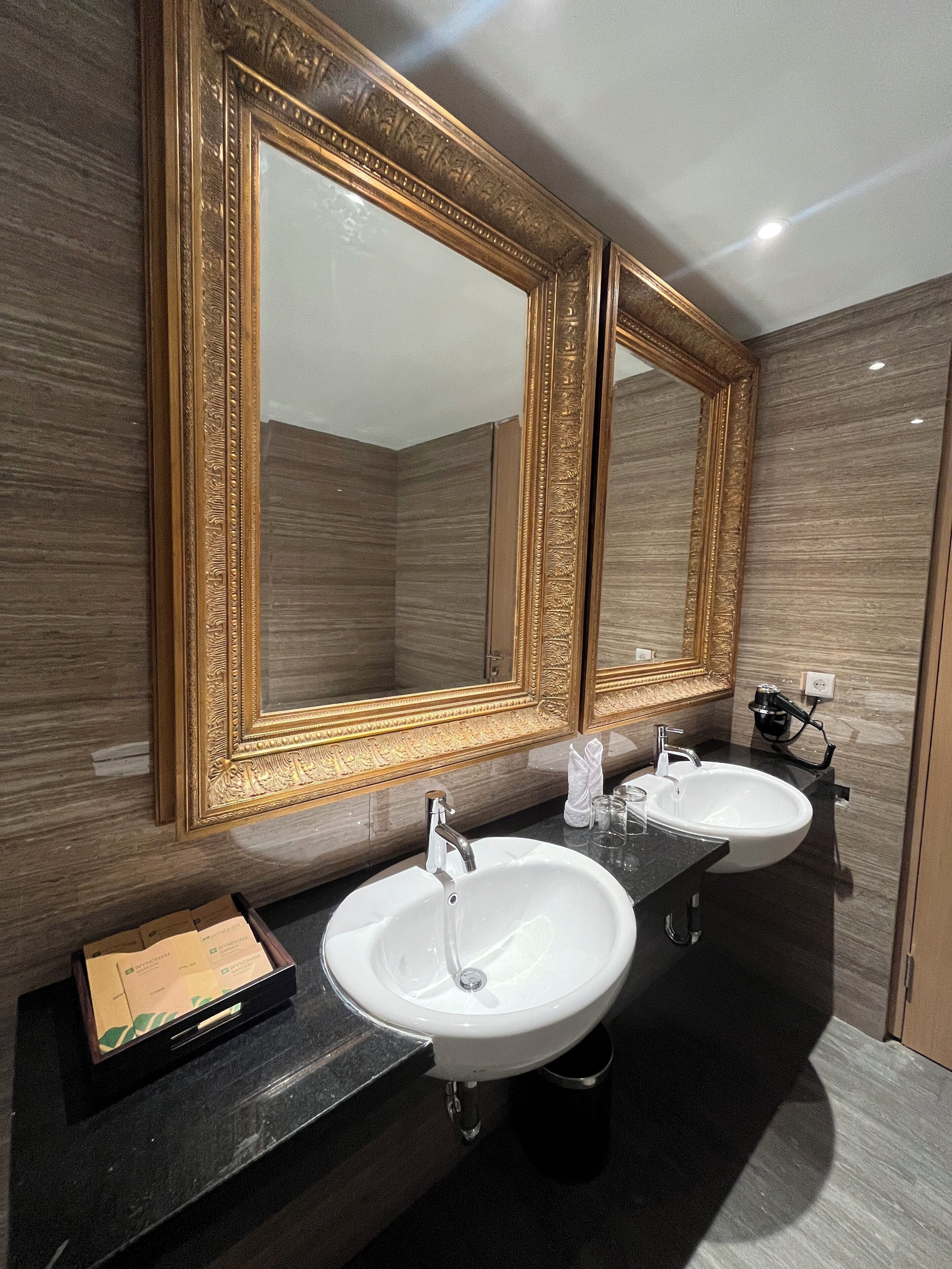 Un baño con dos lavamanos, un espejo grande y un dispensador de toallas.