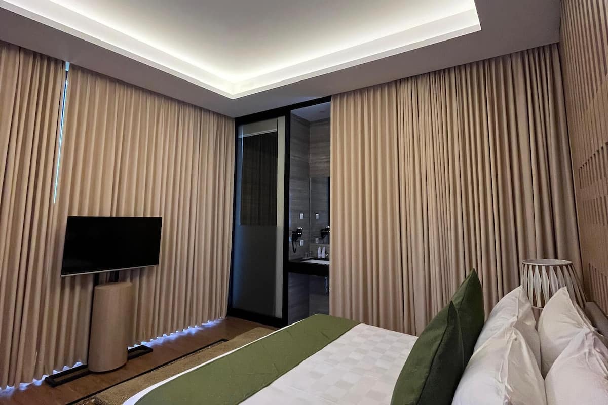 Una habitación de hotel moderna con una cama grande, un televisor de pantalla plana en la pared, una mesita de noche y una lámpara.