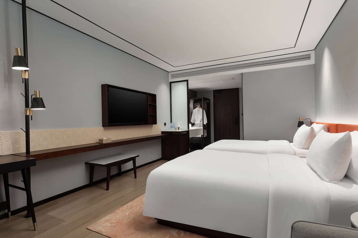A hotel room with a large bed, a desk, a chair, a mirror, and a TV.