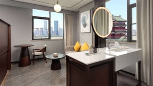 A modern hotel room with a large window offering a city view, a round mirror, a white sink, and a small round table with a chair. - Days Hotel By Wyndham Nanchang Tengwangge (Nanchang)