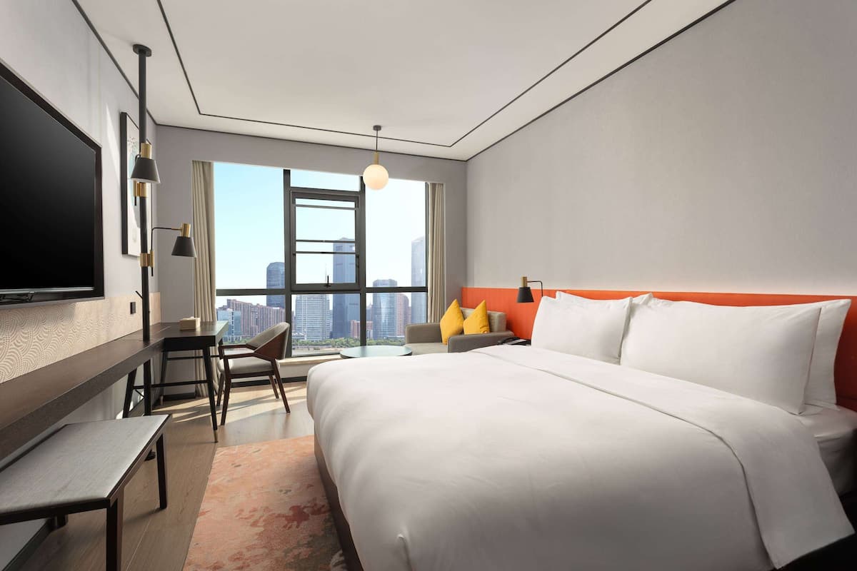 A modern hotel room with a large bed, a desk, and a TV.