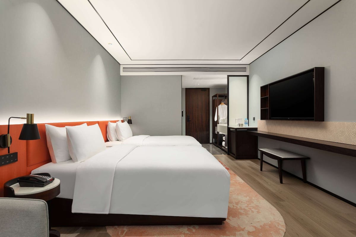A modern hotel room with a large bed, a desk, a flat-screen TV, and a bathroom visible in the background.