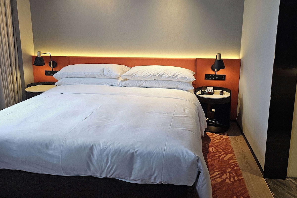A neatly made bed with white linens, two bedside tables with lamps, and a small clock on one of the tables.