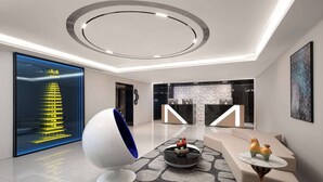 Eine moderne Lobby mit einer zentralen, runden Leuchte, einem Empfangsbereich und einer Sitzecke mit einem ungewöhnlichen, kugelförmigen Sessel und Dekorationselementen.