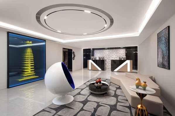 Un hall d’entrée moderne doté d’un luminaire central de forme circulaire, d’un comptoir de réception et d’un espace salon avec un fauteuil sphérique original et des éléments décoratifs.