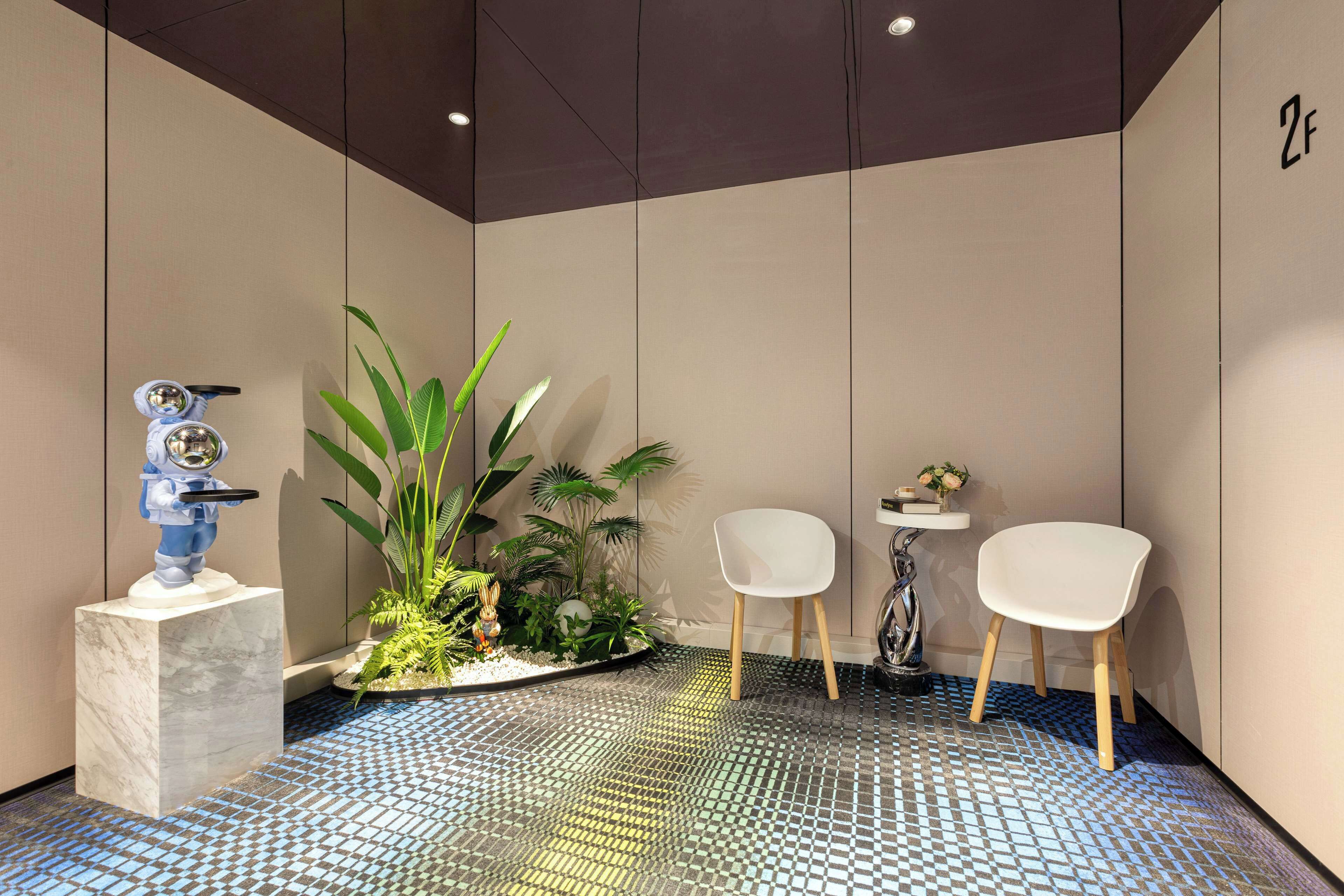 A modern lobby with a tiled floor, a statue, a potted plant arrangement, and two white chairs.