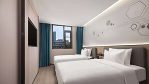 Ein Hotelzimmer mit zwei Betten, einem Flachbildfernseher, einem Nachttisch und Blick auf die Stadt durch große Fenster.