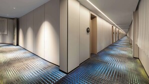 Ein moderner Hotelkorridor mit einem gemusterten Boden, eingelassener Beleuchtung und mehreren Türen.